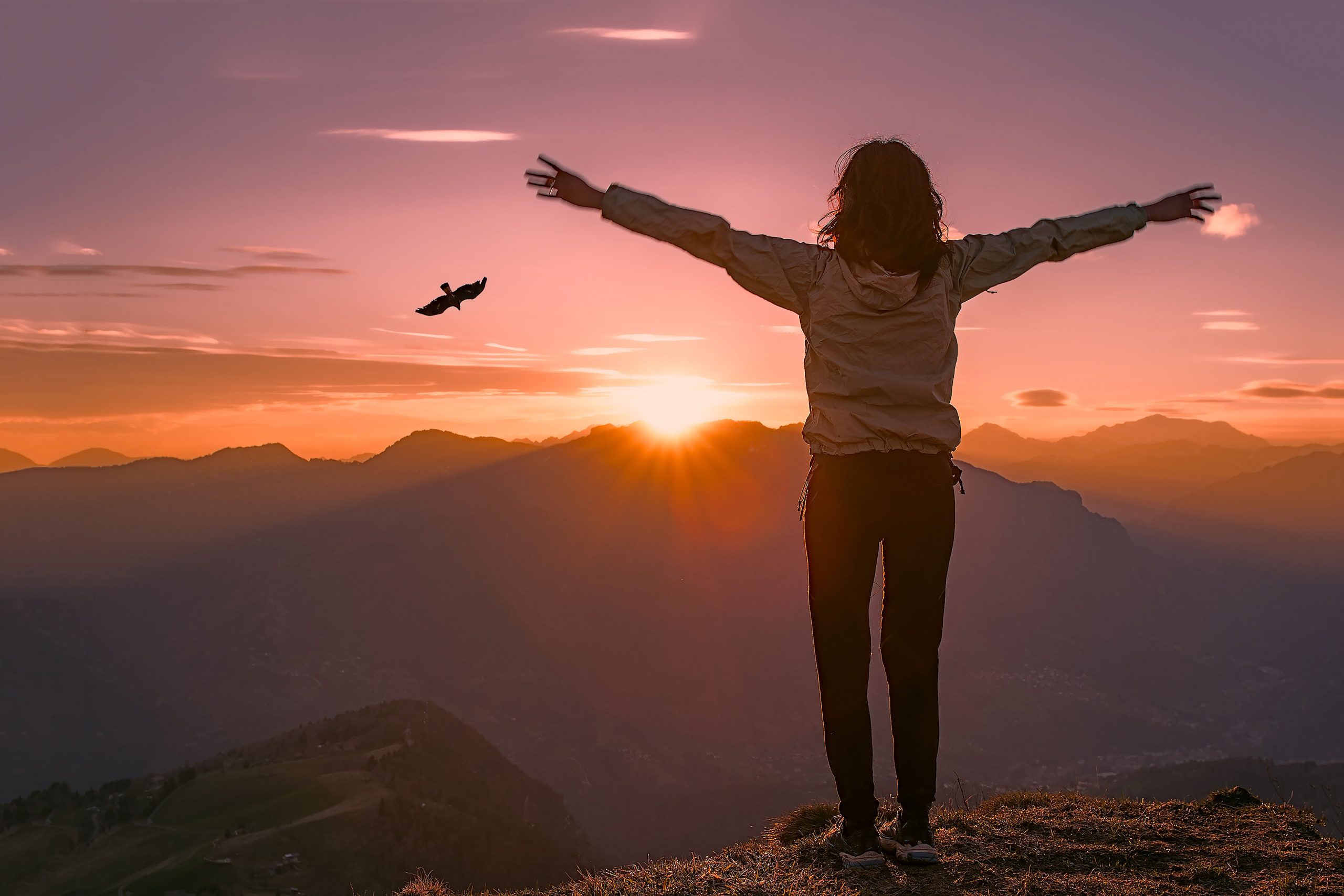 Silhouette of person with outstretched arms on top of a mountain