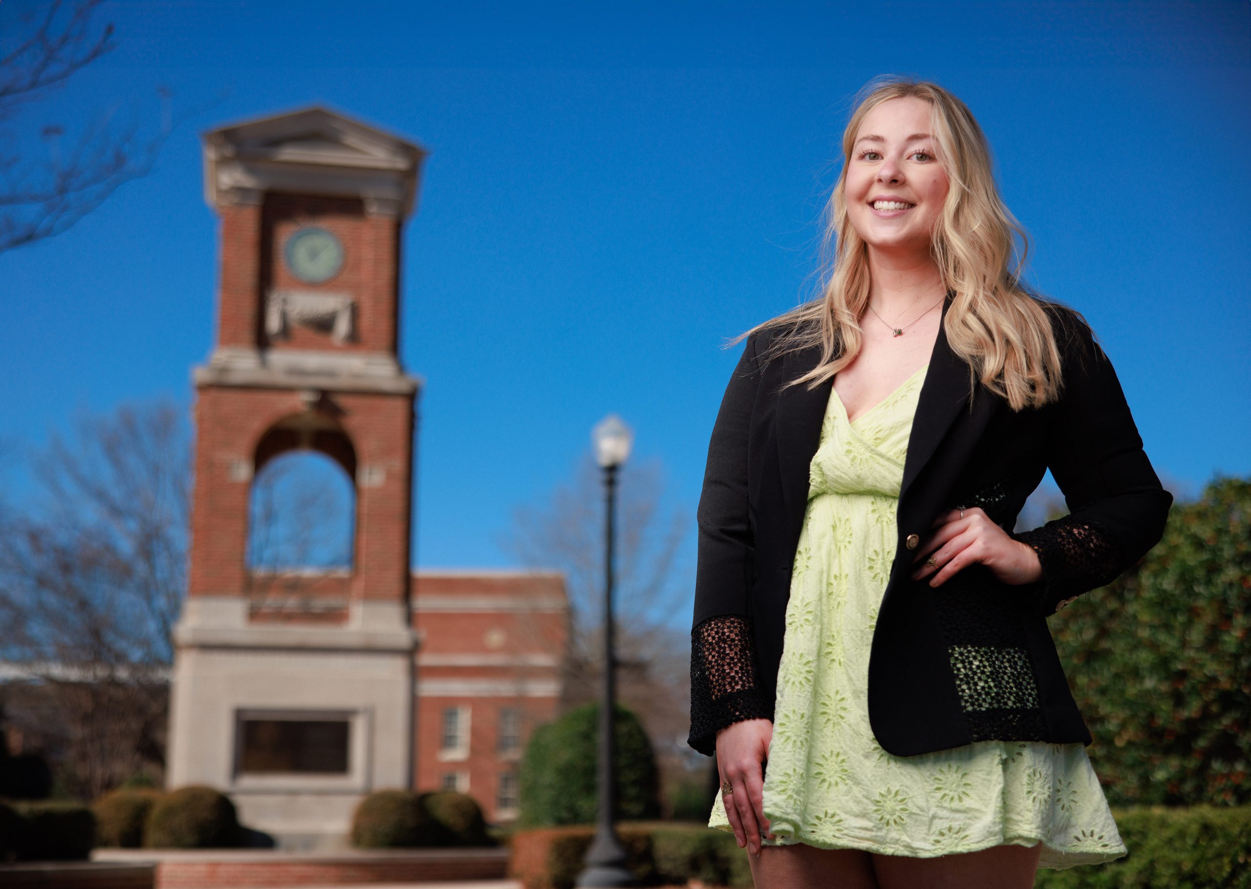 A female college student poses for a photo near a bell tower