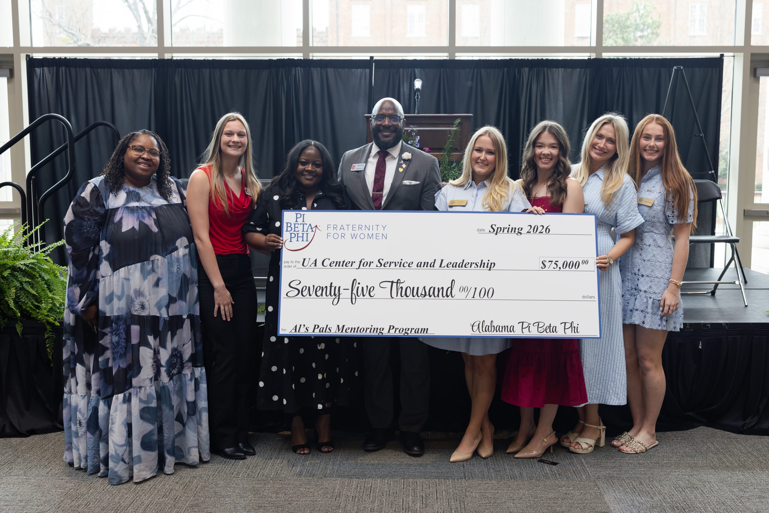 Nine people pose in front of a stage holding an oversized $75,000 check from Pi Beta Phi to the UA Center for Service and Leadership for the Al’s Pals Mentoring Program.